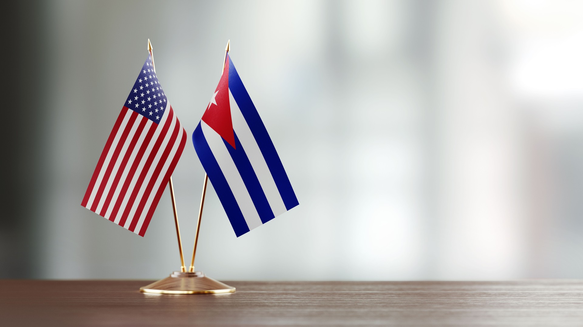 American And Cuban Flag Pair On A Desk Over Defocused Background